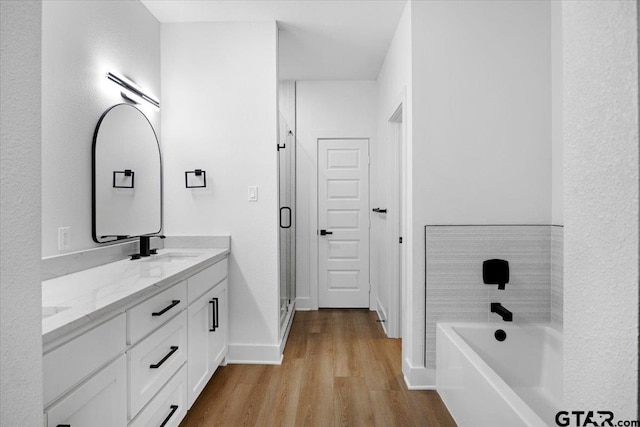 bathroom with double vanity, a sink, a shower stall, wood finished floors, and a bath