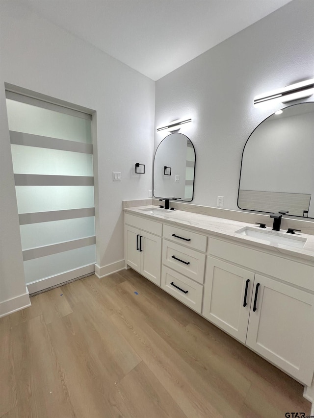 full bath featuring double vanity, baseboards, a sink, and wood finished floors