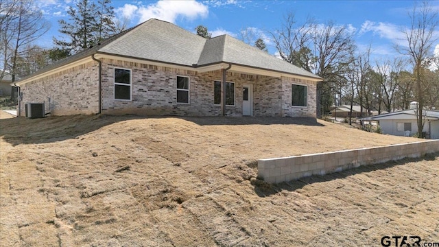 back of house with brick siding, roof with shingles, and central air condition unit