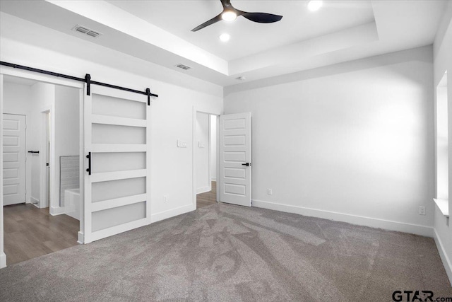 unfurnished bedroom with a barn door, visible vents, a tray ceiling, and carpet flooring