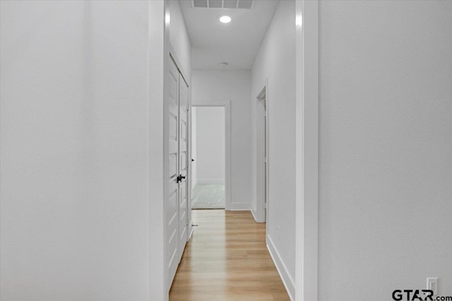 hallway with light wood-style flooring, visible vents, and baseboards