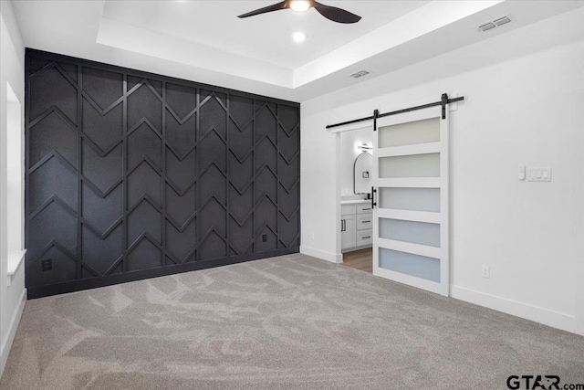 unfurnished bedroom featuring carpet, a raised ceiling, visible vents, a barn door, and an accent wall