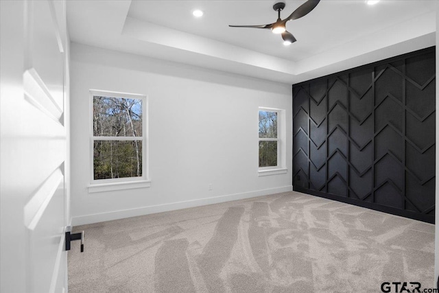 carpeted empty room featuring an accent wall, baseboards, a raised ceiling, and recessed lighting