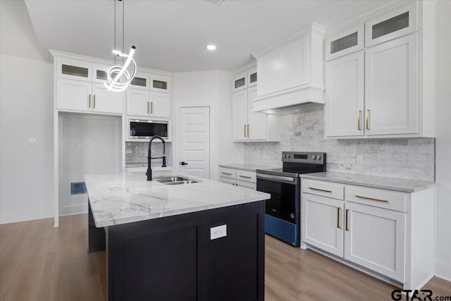 kitchen featuring a sink, appliances with stainless steel finishes, light wood-type flooring, custom exhaust hood, and an island with sink