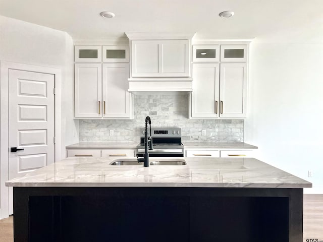 kitchen with light stone counters, a sink, white cabinets, backsplash, and an island with sink