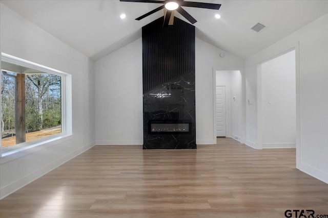 unfurnished living room with light wood-style flooring, a premium fireplace, visible vents, baseboards, and vaulted ceiling