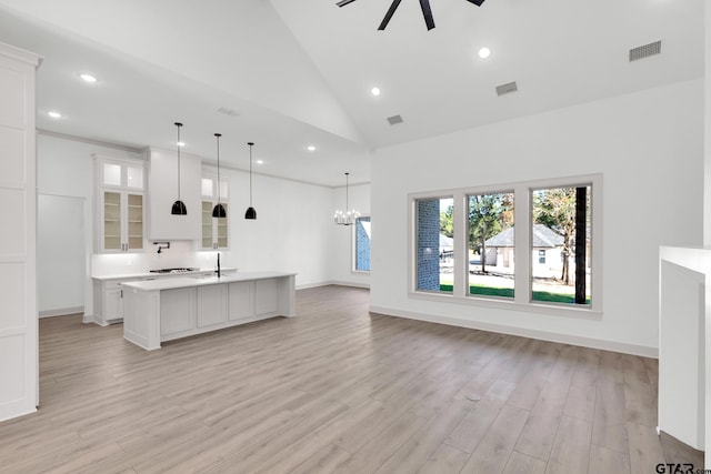 kitchen with decorative light fixtures, white cabinetry, a kitchen island with sink, light wood-type flooring, and high vaulted ceiling