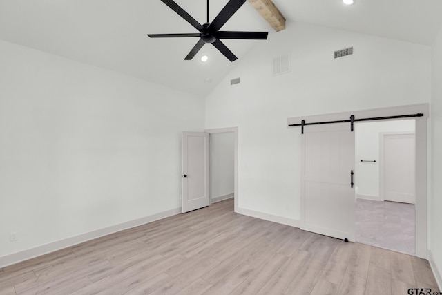 spare room with ceiling fan, a barn door, beamed ceiling, light hardwood / wood-style flooring, and high vaulted ceiling