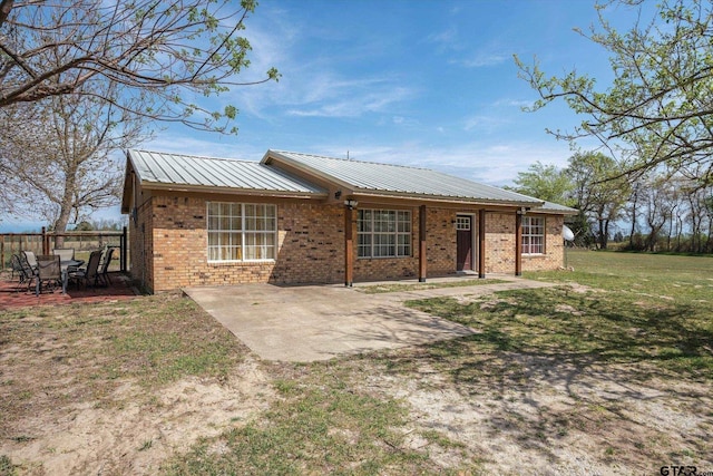 view of front facade featuring brick siding, a front lawn, metal roof, and a patio area
