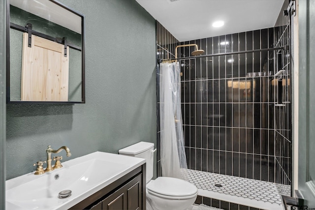 full bath featuring toilet, vanity, a textured wall, and a stall shower