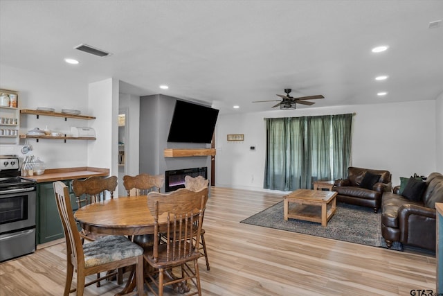 dining space with light wood-type flooring, recessed lighting, visible vents, a glass covered fireplace, and ceiling fan
