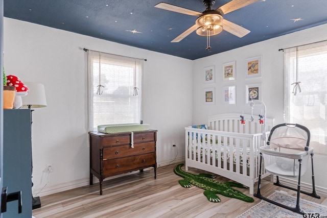 bedroom featuring a nursery area, baseboards, and wood finished floors
