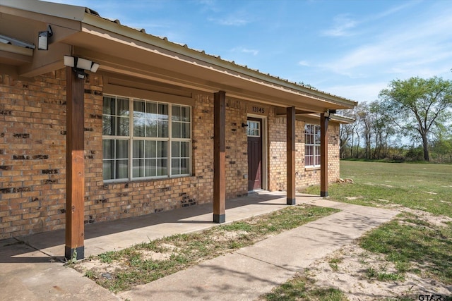 entrance to property with covered porch, brick siding, and a yard