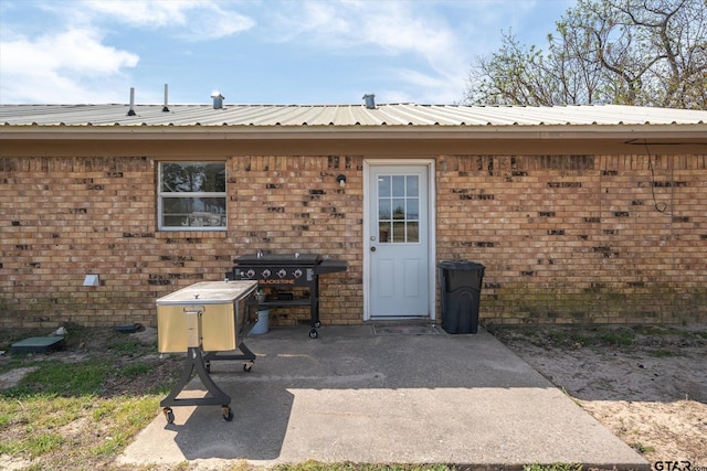 doorway to property featuring a patio, brick siding, and metal roof