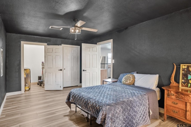 bedroom with light wood-style flooring, baseboards, ceiling fan, and a textured ceiling