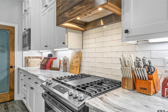 kitchen with tasteful backsplash, premium range hood, light stone counters, stainless steel appliances, and white cabinetry