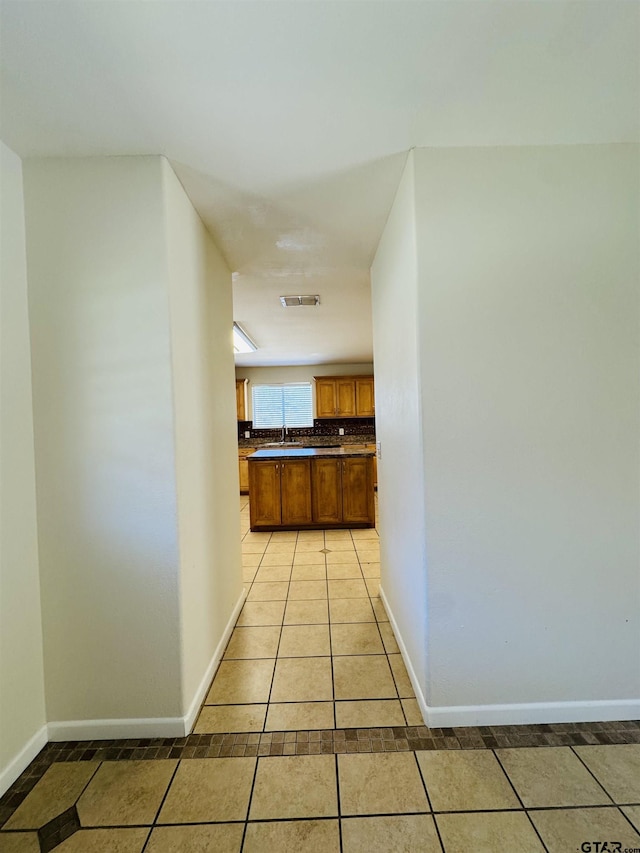 hall featuring light tile patterned flooring, visible vents, baseboards, and a sink