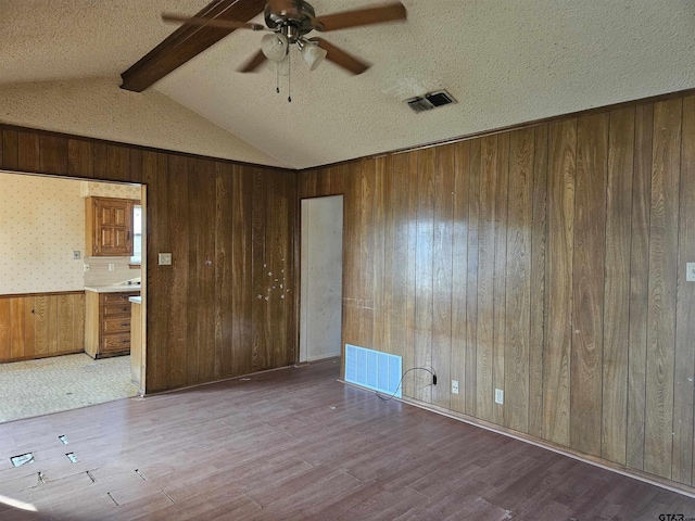 empty room featuring lofted ceiling with beams, visible vents, and wood finished floors