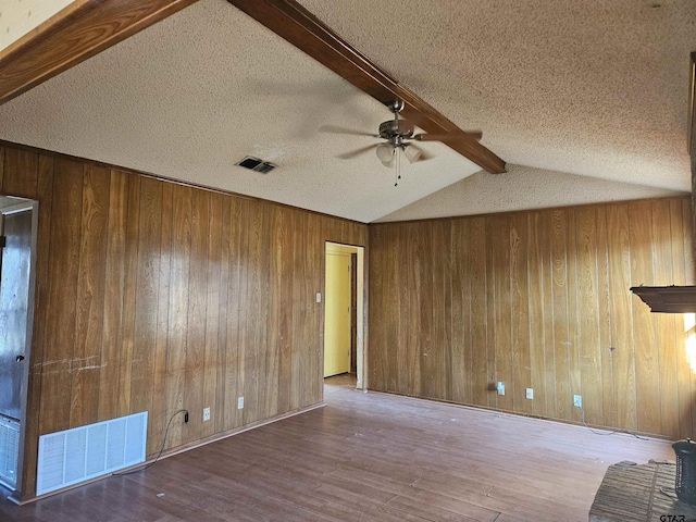 empty room featuring visible vents, lofted ceiling with beams, a ceiling fan, wooden walls, and wood finished floors