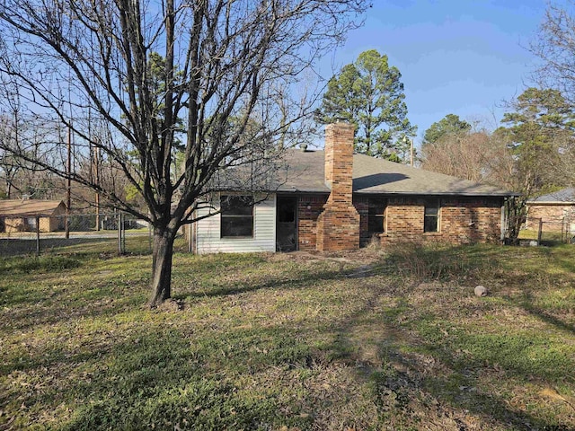 rear view of property featuring a shingled roof, brick siding, fence, and a chimney