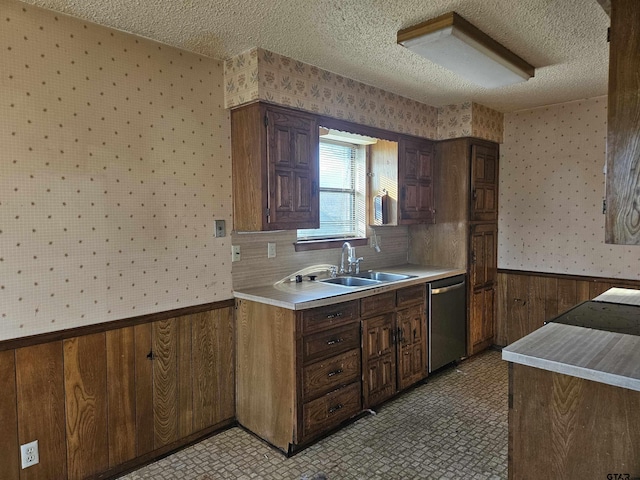 kitchen featuring a wainscoted wall, a sink, a textured ceiling, dishwasher, and wallpapered walls