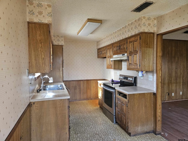 kitchen featuring a wainscoted wall, stainless steel electric stove, a sink, a textured ceiling, and wallpapered walls