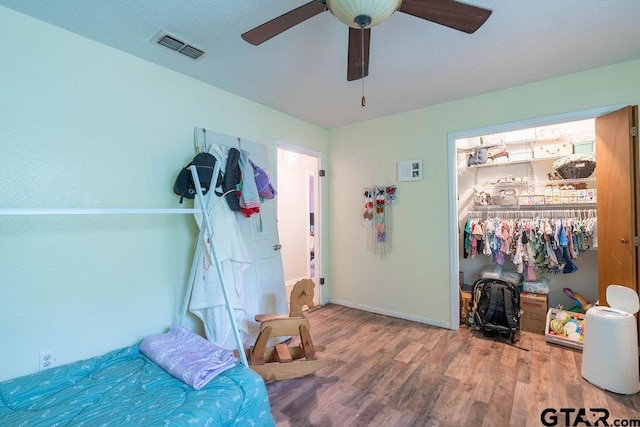 bedroom with a ceiling fan, visible vents, wood finished floors, baseboards, and a closet