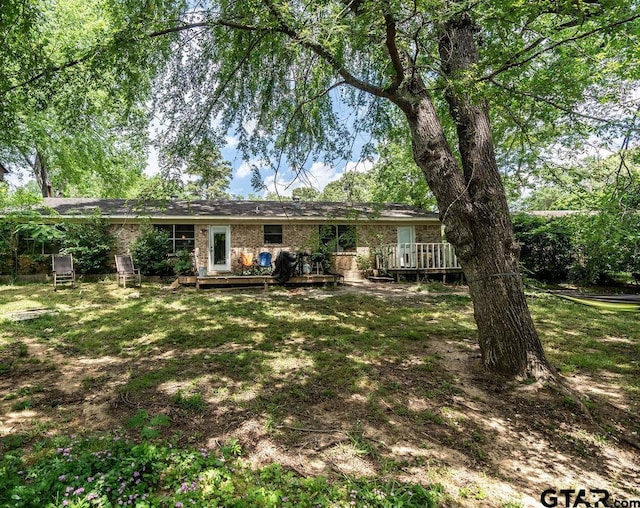 rear view of house with brick siding, a lawn, and a deck