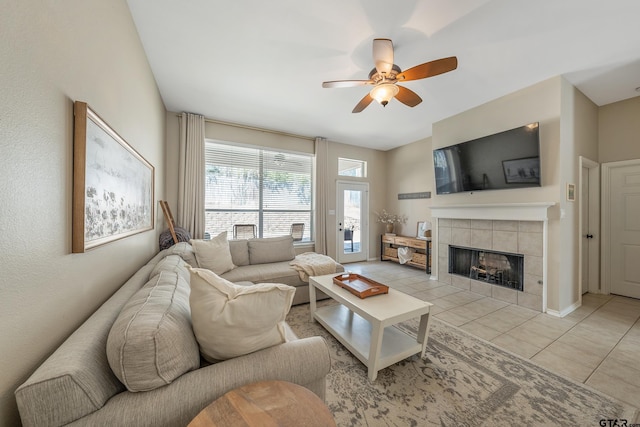 living room with a ceiling fan, a tile fireplace, baseboards, and light tile patterned floors