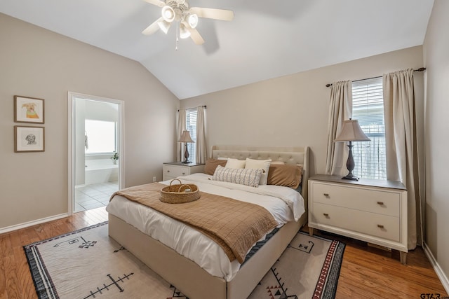 bedroom featuring a ceiling fan, vaulted ceiling, ensuite bath, light wood-type flooring, and baseboards