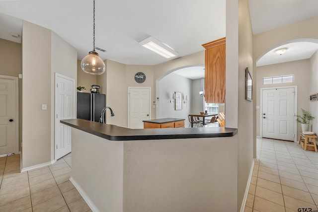 kitchen with arched walkways, light tile patterned floors, a kitchen island, freestanding refrigerator, and dark countertops