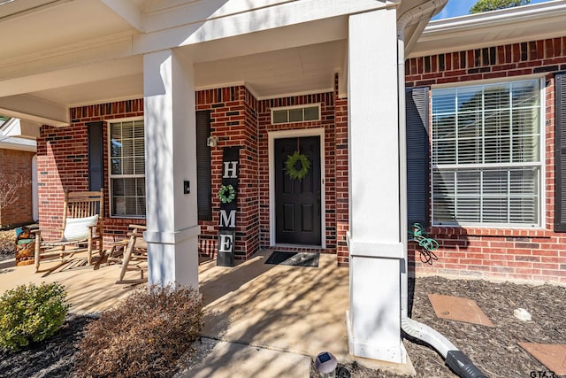 view of exterior entry featuring covered porch and brick siding