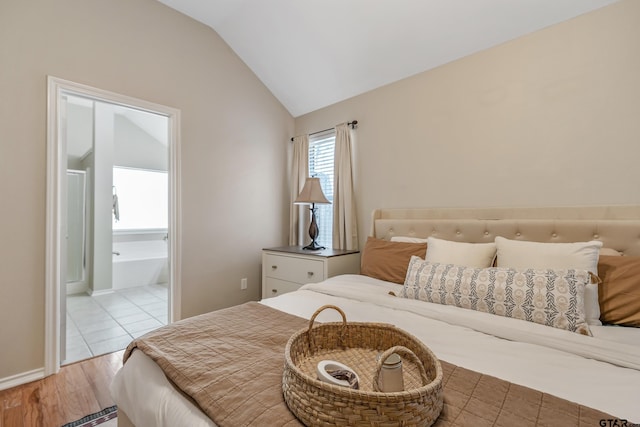 bedroom with lofted ceiling, light wood-style floors, and ensuite bath