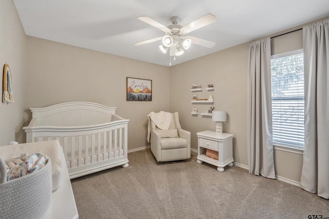 bedroom with a crib, baseboards, a ceiling fan, and carpet flooring