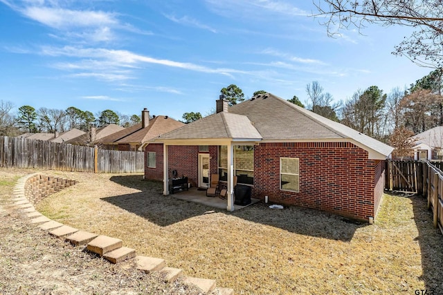 rear view of property featuring a patio area, a fenced backyard, a chimney, and brick siding