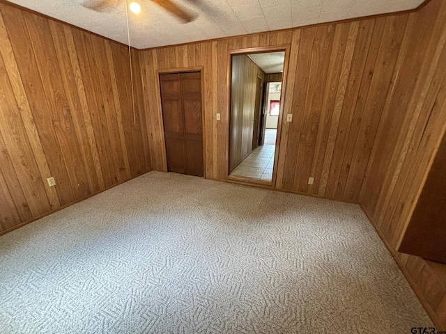 spare room with a textured ceiling, light colored carpet, wood walls, and ceiling fan