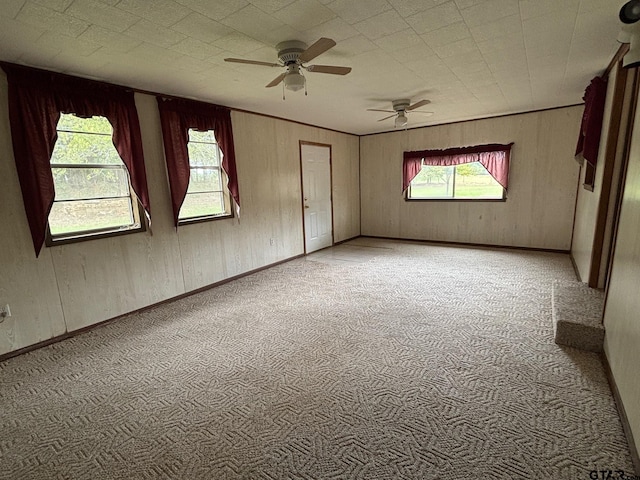 carpeted empty room featuring a wealth of natural light, ceiling fan, and wooden walls