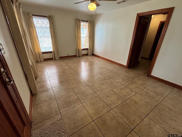 tiled empty room with ceiling fan, a healthy amount of sunlight, and a textured ceiling