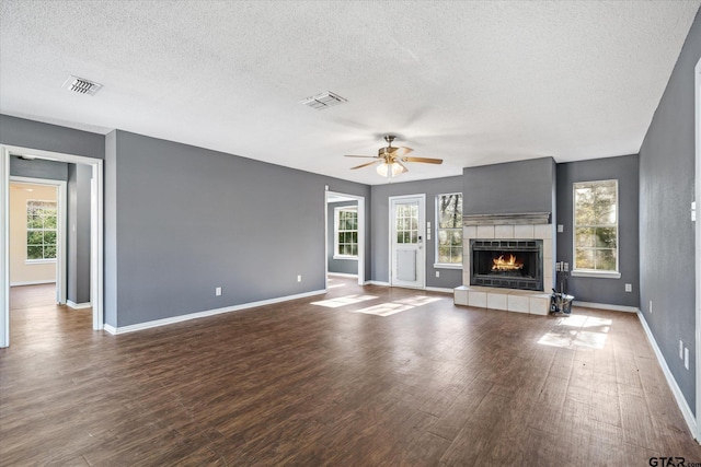 unfurnished living room featuring hardwood / wood-style floors, a healthy amount of sunlight, a textured ceiling, and a tiled fireplace