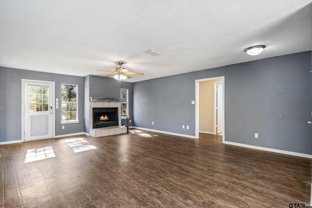 unfurnished living room with a textured ceiling, dark hardwood / wood-style floors, ceiling fan, and a tiled fireplace