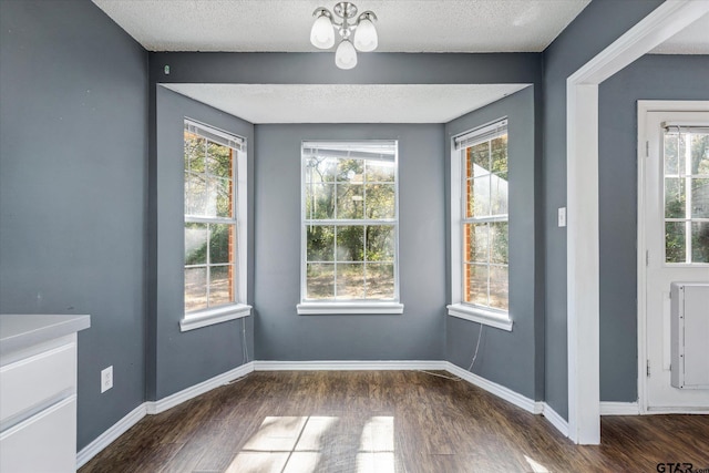 unfurnished dining area with a chandelier, a textured ceiling, and dark hardwood / wood-style floors