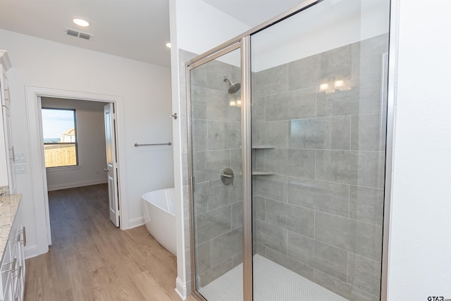 bathroom featuring visible vents, a freestanding tub, a shower stall, wood finished floors, and vanity