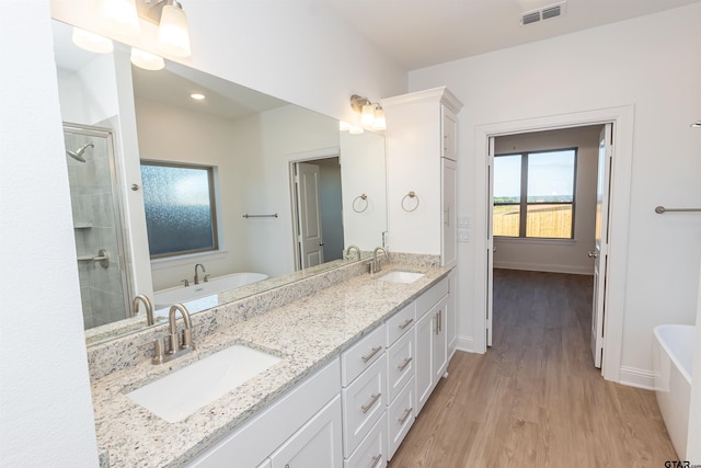 full bathroom with visible vents, a sink, wood finished floors, and a tub to relax in
