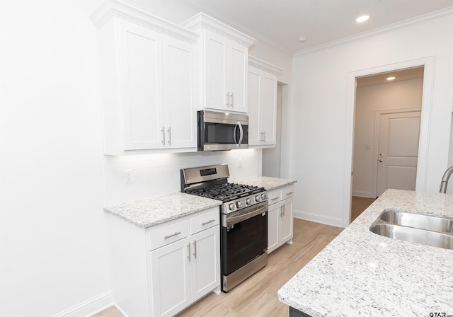 kitchen featuring appliances with stainless steel finishes, a sink, baseboards, decorative backsplash, and light wood-type flooring