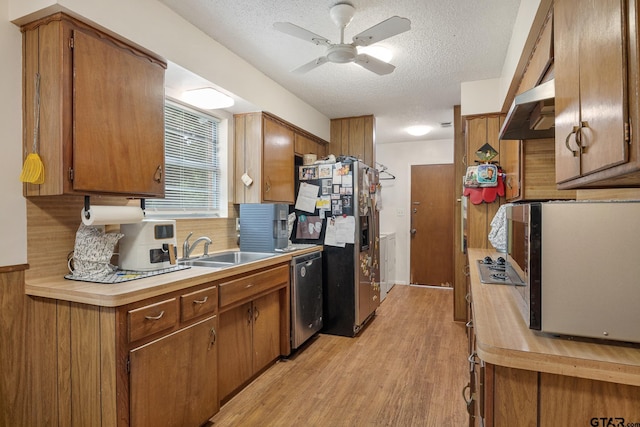 9961 Creek Bend Dr, Tyler, TX 75707 - kitchen with stainless steel appliances, a sink, under cabinet range hood, a textured ceiling, and light wood-style flooring