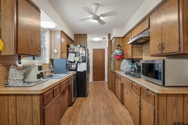 9961 Creek Bend Dr, Tyler, TX 75707 - kitchen with appliances with stainless steel finishes, a sink, under cabinet range hood, a textured ceiling, and light wood-type flooring