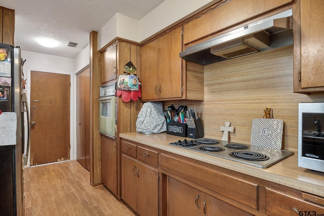 9961 Creek Bend Dr, Tyler, TX 75707 - kitchen with appliances with stainless steel finishes, under cabinet range hood, light countertops, brown cabinetry, and a textured ceiling