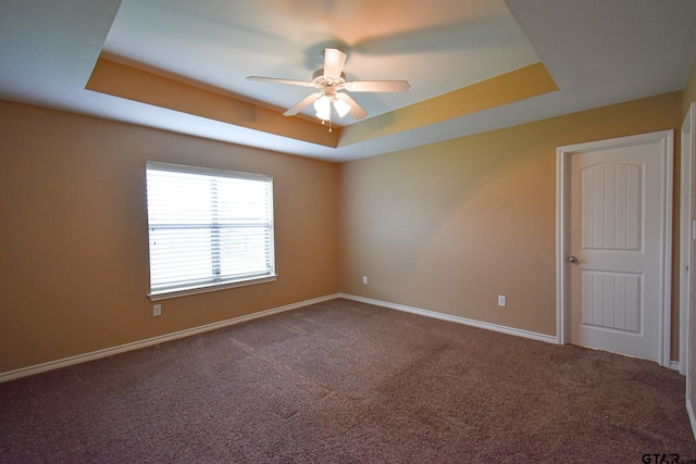 empty room with carpet flooring, ceiling fan, and a tray ceiling