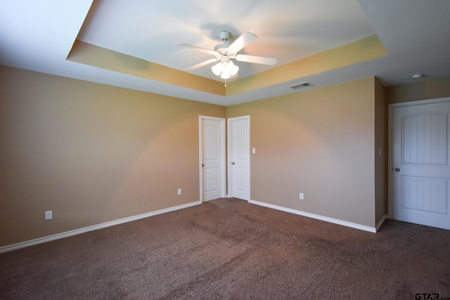 unfurnished bedroom featuring dark colored carpet, ceiling fan, and a raised ceiling