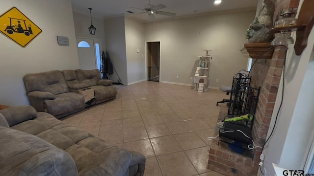 living room featuring light tile patterned floors, ceiling fan, a towering ceiling, ornamental molding, and a brick fireplace